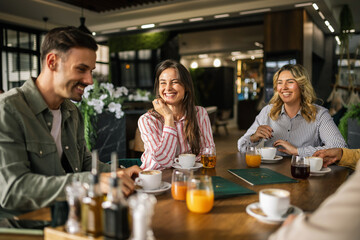 Group of young people sitting at a table in a modern café, enjoying their time together with cups of coffee and glasses of freshly squeezed juice.