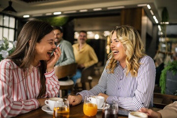 Group of female friends drinking coffee at the restaurant while the guys in the back try to flirt and send them drinks.