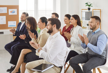 Group of happy joyful business people applauding to speaker sitting on chairs in a meeting room. Successful coworkers and company employees clapping a colleague on business training or conference.