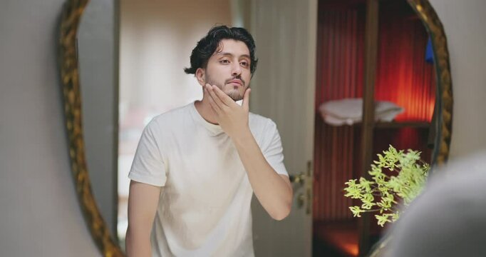 Indian Asian gen z young adult single happy man male guy smiling look mirror touch beard daily care routine feel proud shows good comb hair with finger ready for new day Joyful enjoy indoor house