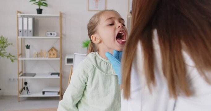 Dentist or ENT doctor examines the teeth or throat of a young girl patient in a clinic. Healthcare consultation of patient emphasizes child health, thorough dentistry, and professional care.