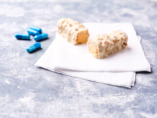 Protein bar in two pieces and amino acids capsules on wooden background. Soft focus. Close up. Copy space