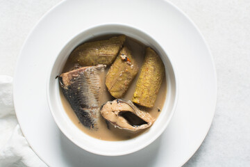 Overhead view of Nigerian pepper soup with fish and plantain in a white soup plate, top view of fish pepper soup in a white plate
