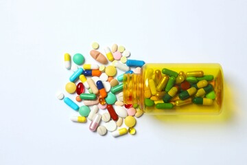 Various pills pouring out of medicine bottle on white background