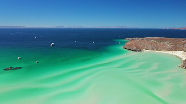 Boats approach a tropical island featuring white sand beaches and stunning turquoise waters under a clear blue sky. Balandra beach in Mexico, drone view