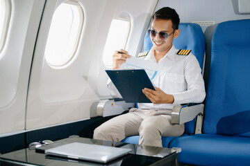 Asian Confident male pilot in uniform leaning at the passenger seat while standing inside of the...