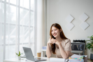 A woman is sitting at a desk with a laptop and a stack of papers