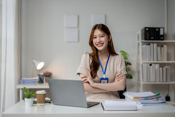 A woman is sitting at a desk with a laptop and a stack of papers