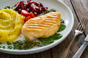 Grilled chicken breast, mashed potatoes and fresh vegetables on wooden table	