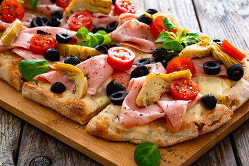 Roman Pizza with mozzarella cheese, boiled ham, cherry tomatoes, black olives and artichokes on wooden table