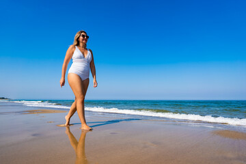 Summertime by sea. Beautiful middle-aged woman walking on sandy beach on sunny summer day. Front view