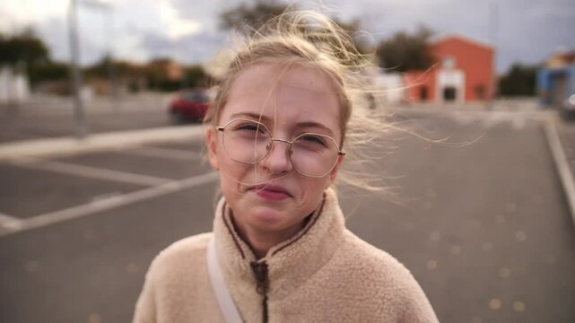 Young girl in beige coat smiling at camera with windswept hair, ideal for winter fashion campaigns, lifestyle blogs, personal branding materials and seasonal style content