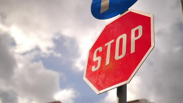 Stop sign with blue directional arrow against cloudy sky, perfect for road safety campaigns, driver education materials, traffic regulation content and urban infrastructure presentations