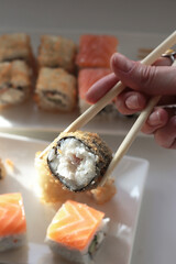 set of rolls and sushi with fish, breaded, rice, Japanese food, Japanese food delivery, bright rolls, hand holding chopsticks with roll, California, Philadelphia, white dishes, soy sauce