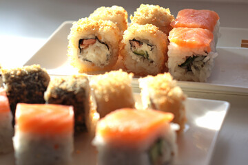 set of rolls and sushi with fish, breaded, rice, Japanese food, Japanese food delivery, bright rolls, hand holding chopsticks with roll, California, Philadelphia, white dishes, soy sauce
