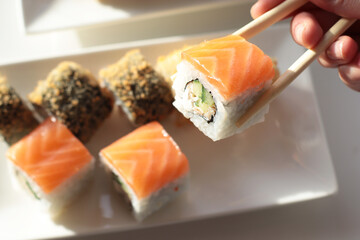 set of rolls and sushi with fish, breaded, rice, Japanese food, Japanese food delivery, bright rolls, hand holding chopsticks with roll, California, Philadelphia, white dishes, soy sauce