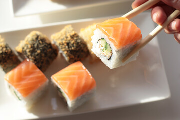 set of rolls and sushi with fish, breaded, rice, Japanese food, Japanese food delivery, bright rolls, hand holding chopsticks with roll, California, Philadelphia, white dishes, soy sauce
