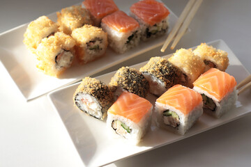 set of rolls and sushi with fish, breaded, rice, Japanese food, Japanese food delivery, bright rolls, hand holding chopsticks with roll, California, Philadelphia, white dishes, soy sauce