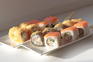 set of rolls and sushi with fish, breaded, rice, Japanese food, Japanese food delivery, bright rolls, hand holding chopsticks with roll, California, Philadelphia, white dishes, soy sauce
