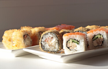 set of rolls and sushi with fish, breaded, rice, Japanese food, Japanese food delivery, bright rolls, hand holding chopsticks with roll, California, Philadelphia, white dishes, soy sauce
