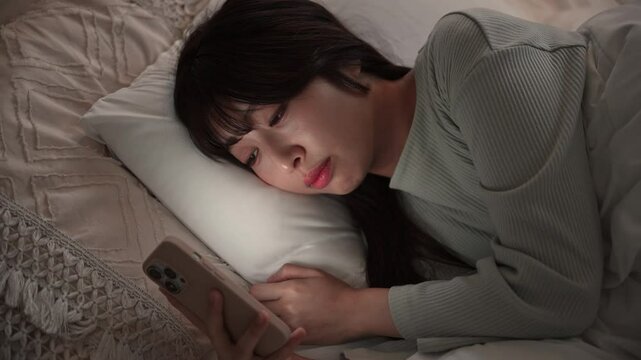 夜中にスマホを見て睡眠が足りず寝不足になってしまう女性のクローズアップでタップする動画　ニュートラルなカラー