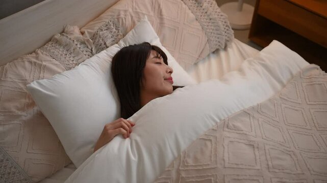 間接照明で眠りにつく女性　ベッドの睡眠や安眠のイメージのクローズアップの動画　ニュートラルな色俯瞰