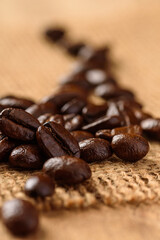 Close up of roasted coffee beans on brown woven sackcloth. Selective focus on blurred background.