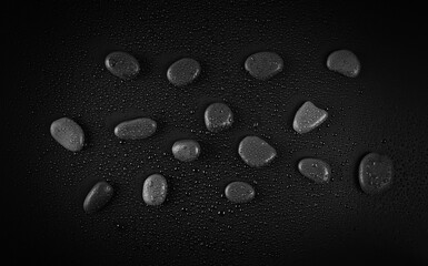 Oval stones with water drops on black background, top view