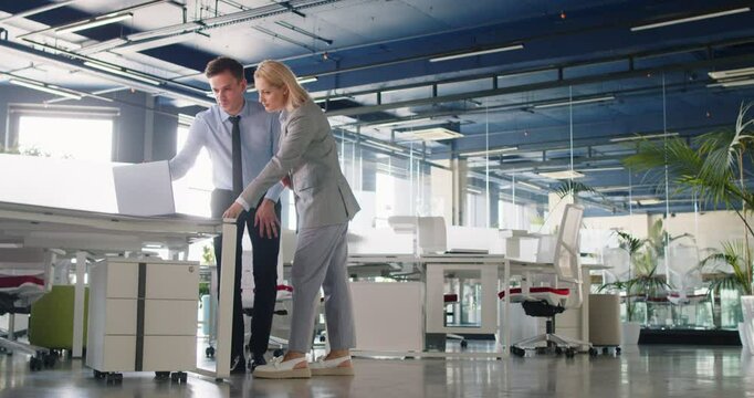 Company employees discussing project details, working on collaborative task. Man and woman walking through modern office, approaching desk, looking at some data on laptop screen, analyzing results.