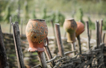 Traditional ukrainian clay pots on a wicker fence. Wooden fence in a countryside with ceramic pots hanging on top (close-up selective focus).