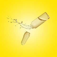 Open ampoule with splashing liquid in air on yellow background