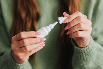 Woman holding a small medicine bottle with liquid eyes or ears drops. Close-up of medical...