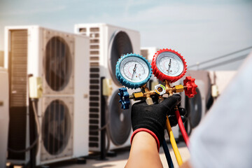 Electrical conditioning service technician using measuring manifold gauge checking HVAC condition system and refrigerant filling air conditioner after cleaning and maintenance compressor units.