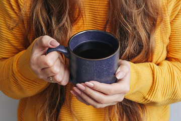 Woman in a yellow sweater holding a cup of coffee. Enjoying a hot beverage at home during...