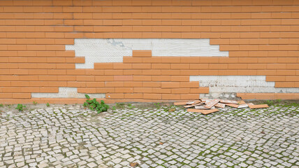 Broken brick tiles falling from building facade onto cobblestone street