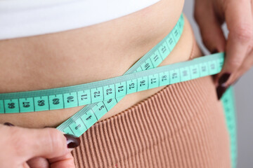 Woman measuring her waist circumference with a tape. Body fat level background. Slim body in sporty...