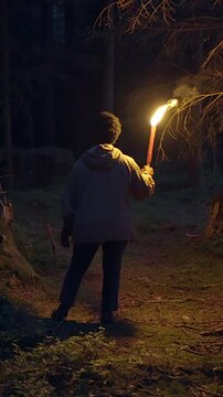 A mysterious figure is seen holding a torch while wandering in a dark and eerie forest