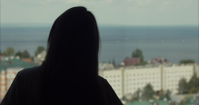 Woman drinking wine and admiring city view from balcony