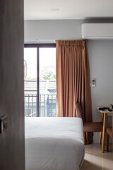Bedroom interior. Large bed and table, lighting from the window with a balcony, air conditioning on the wall