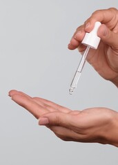 Close-up of female hands on isolated grey background holding pipette dropper, dripping