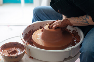 Female hands throwing a large sized bowl on a potter's wheel in a sunlit pottery studio