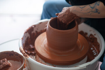 Female hands throwing a large sized bowl on a potter's wheel in a sunlit pottery studio