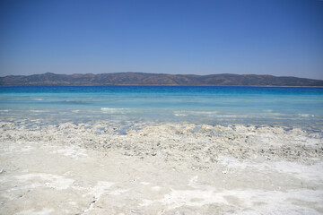a beach with light and dark blue water and mountains in the background