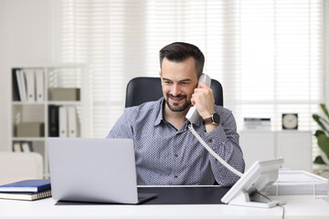 Happy banker talking on phone at table in office