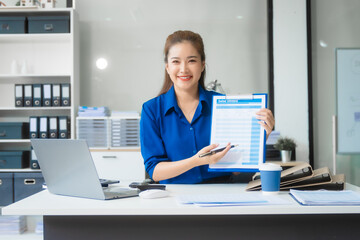 Attractive Asian businesswoman in formal business attire is working at her desk with a laptop and mobile phone, focusing on corporate law, contracts, compliance, and law firm marketing strategies.