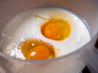 A bowl with yoghurt, two chicken eggs, and other ingredients ready to be mixed and prepare pancake batter