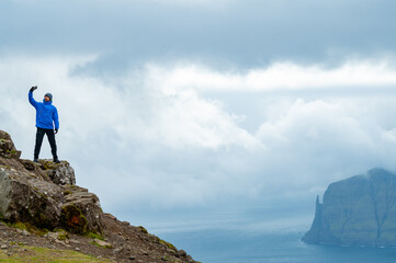 man taking a selfie on top of mountain with dramatic clouds over the mountains of the Faroe Island 