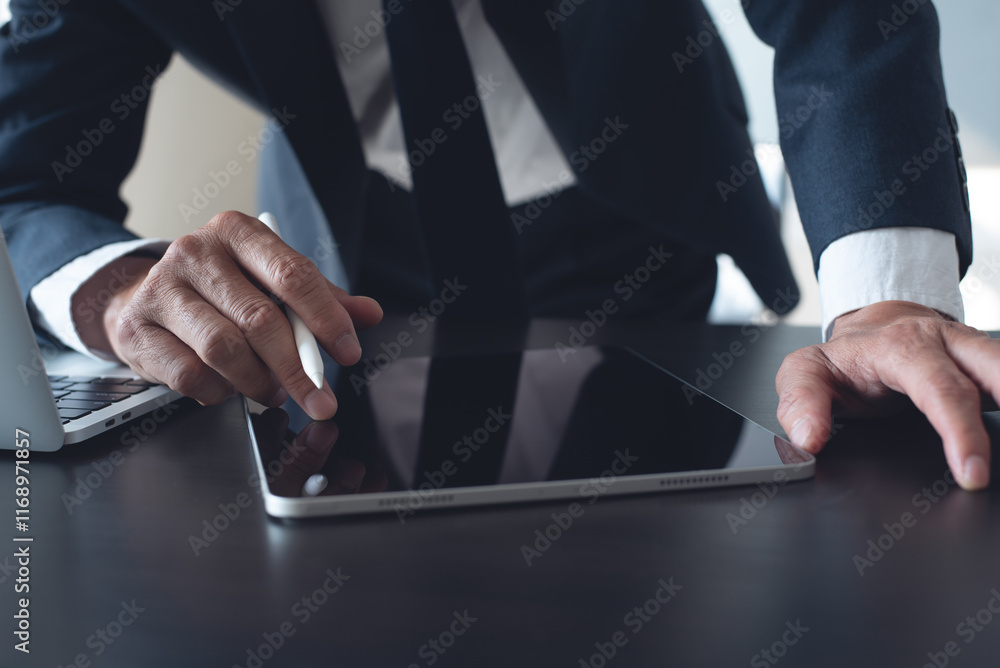 Poster businessman using digital tablet surfing the internet and working on laptop computer on office desk.