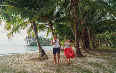 Man with smartphone and woman walking on the beach