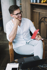 Smiling male journalist holding pen for making notes in notebook while sitting in cafe